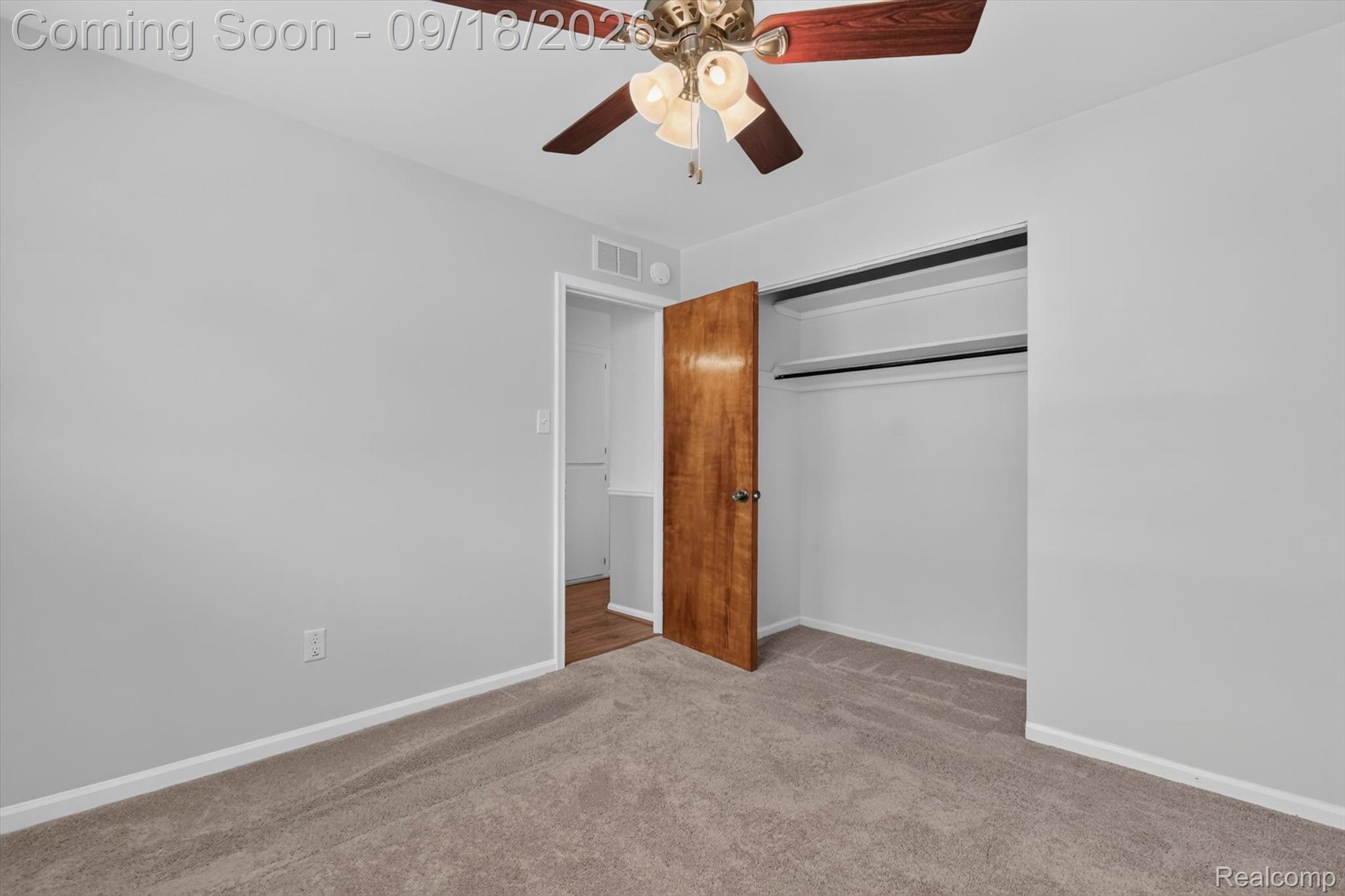 Empty bedroom with taupe carpet, an open closet, and a ceiling fan.