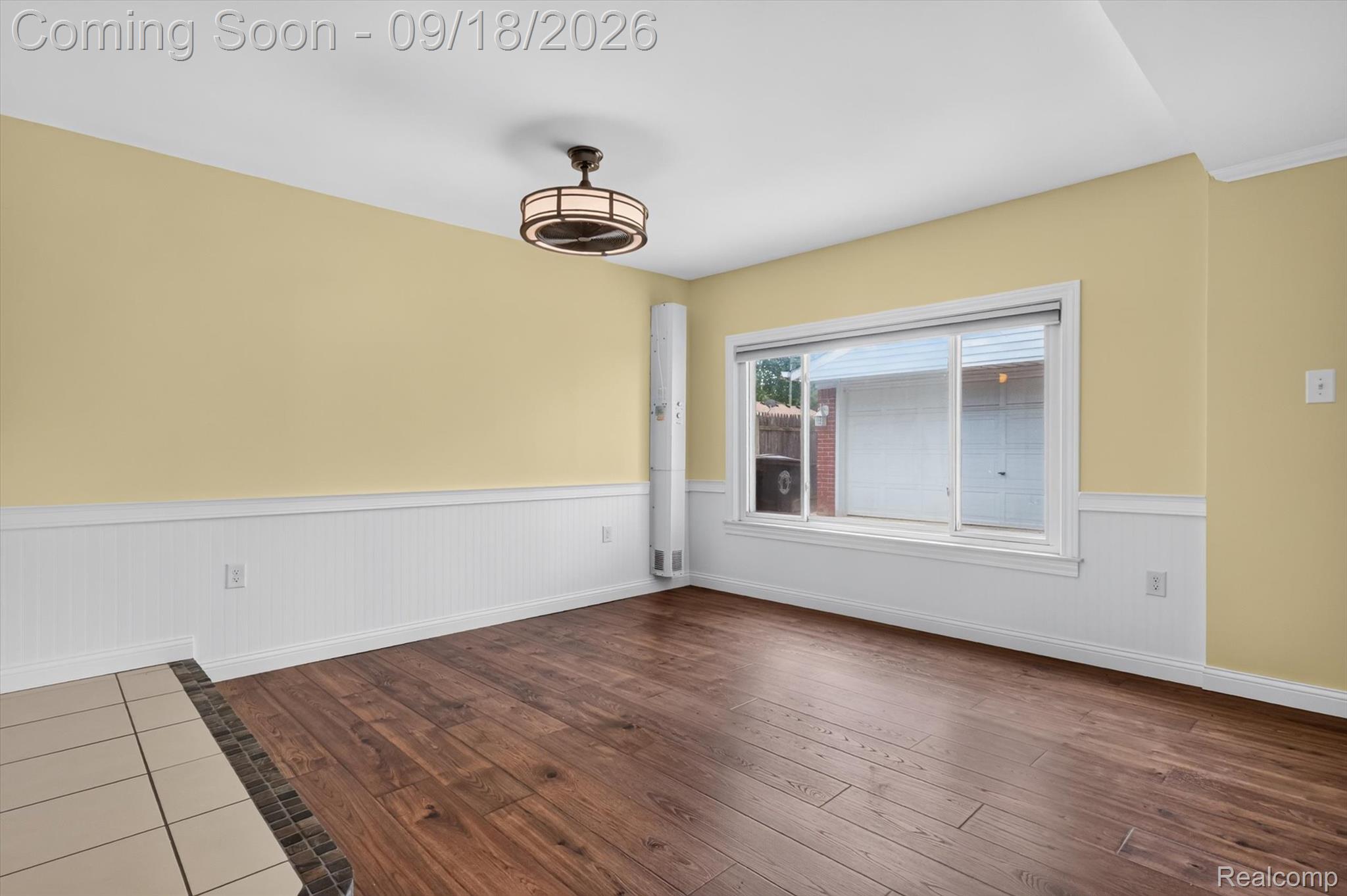 Vacant room with yellow walls, white wainscoting, dark wood floors, and a large window.