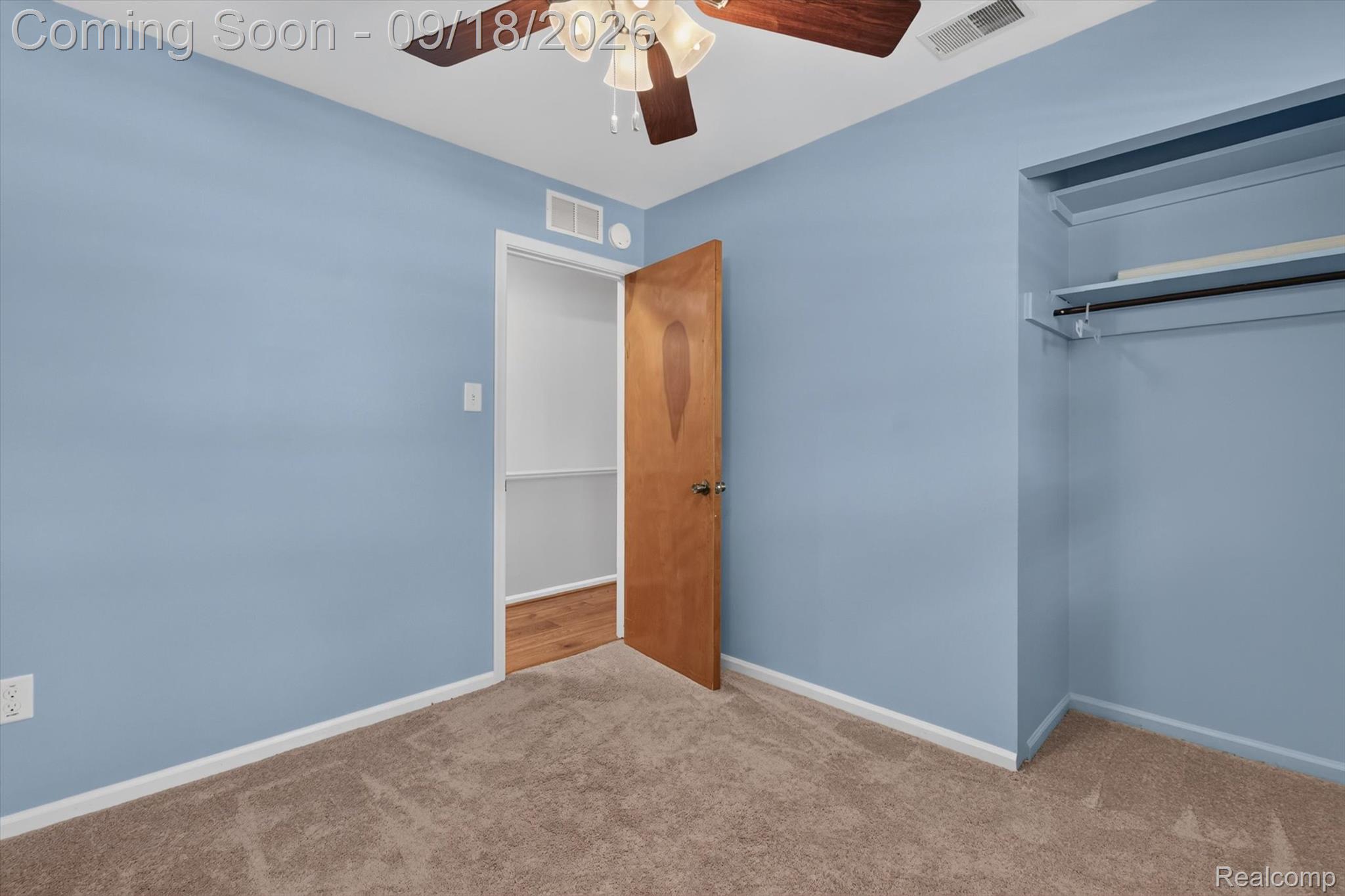 Empty blue bedroom with beige carpet, a ceiling fan, and an open closet.