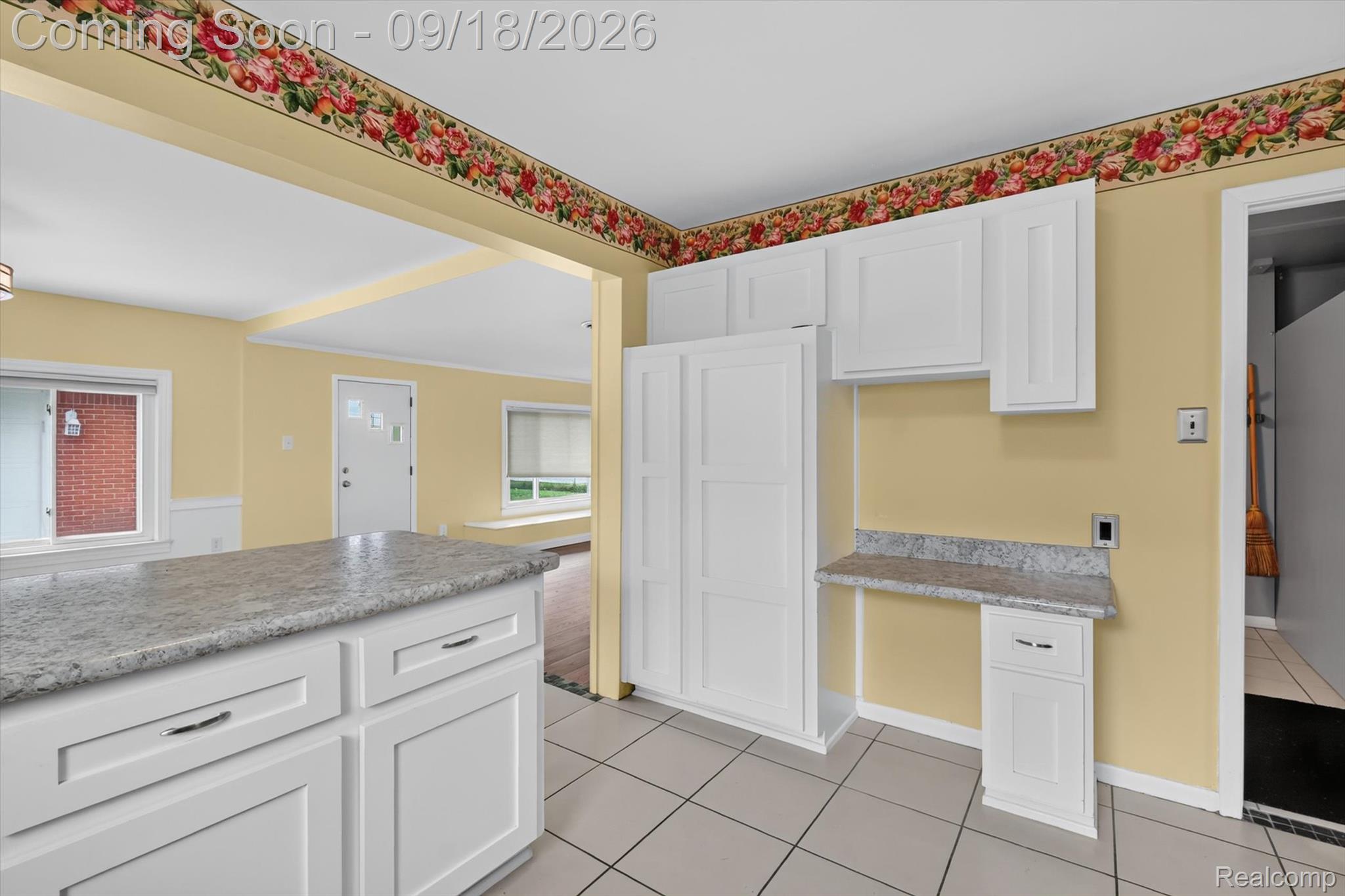 Kitchen with white cabinets, gray stone countertops, and a floral wallpaper border.