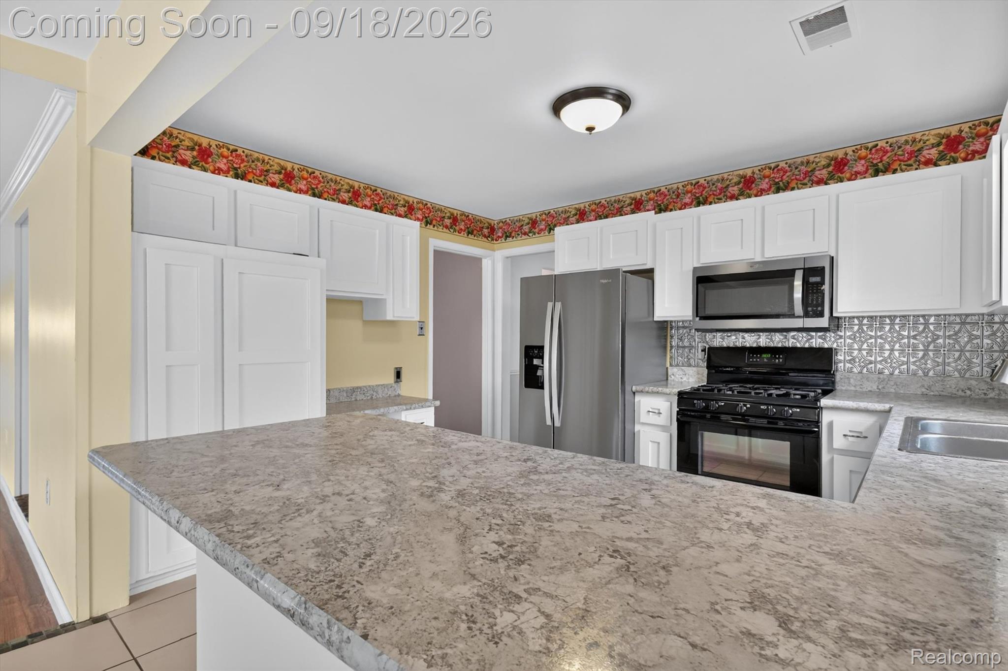 Kitchen with a large granite-pattern island, white cabinets, and stainless steel appliances.
