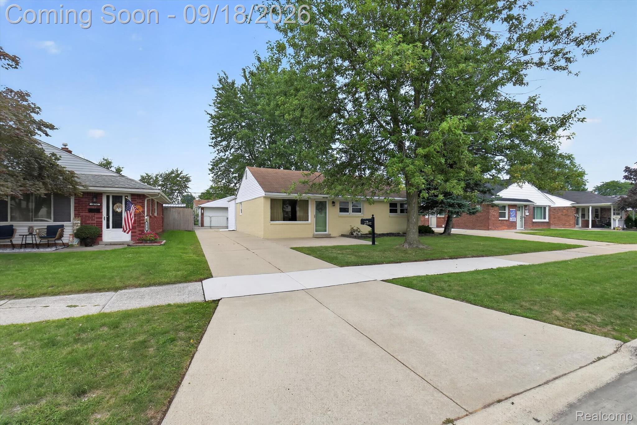 Single-story yellow house with a large front-yard tree and concrete driveway.