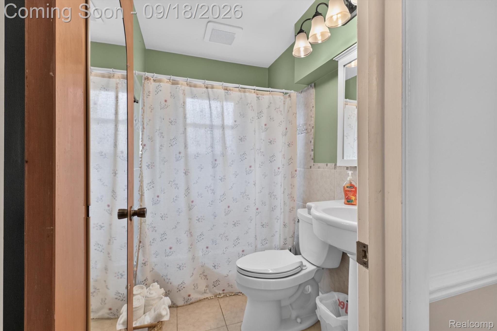Bathroom with a floral shower curtain, green walls, and beige tile.