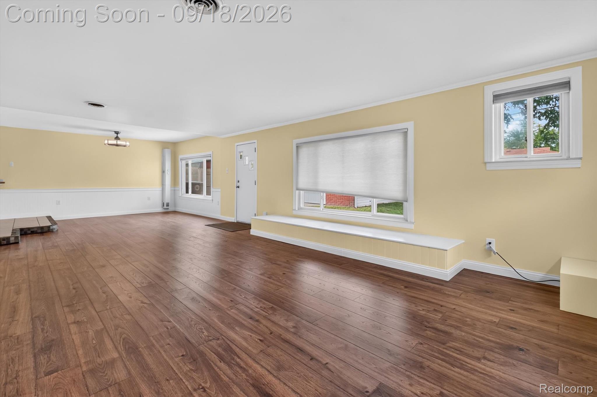 Vacant living room with wide-plank wood floors, yellow walls, and a built-in ledge beneath the front window.