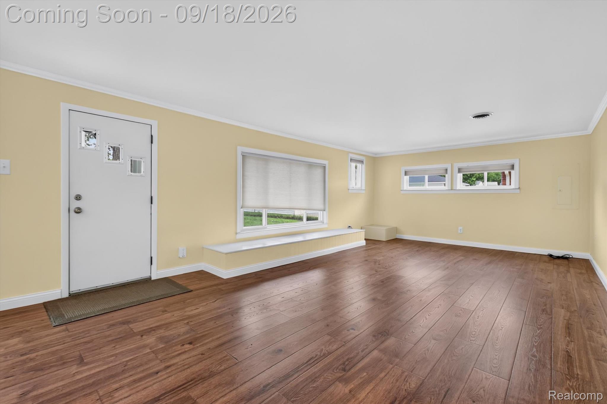 Empty living room with hardwood floors, pale yellow walls, and a white entry door.
