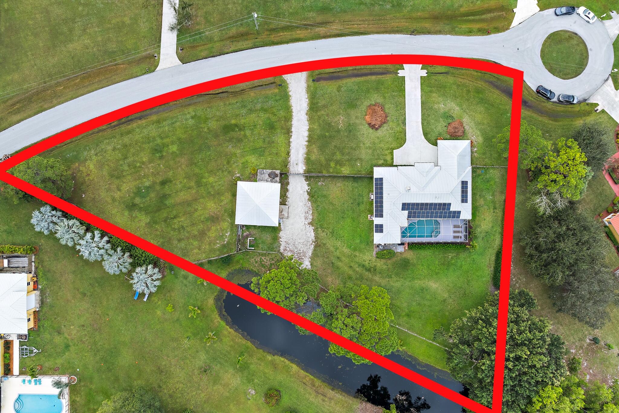 Aerial view of a red-outlined property with a home, screened pool, solar panels, and pond.