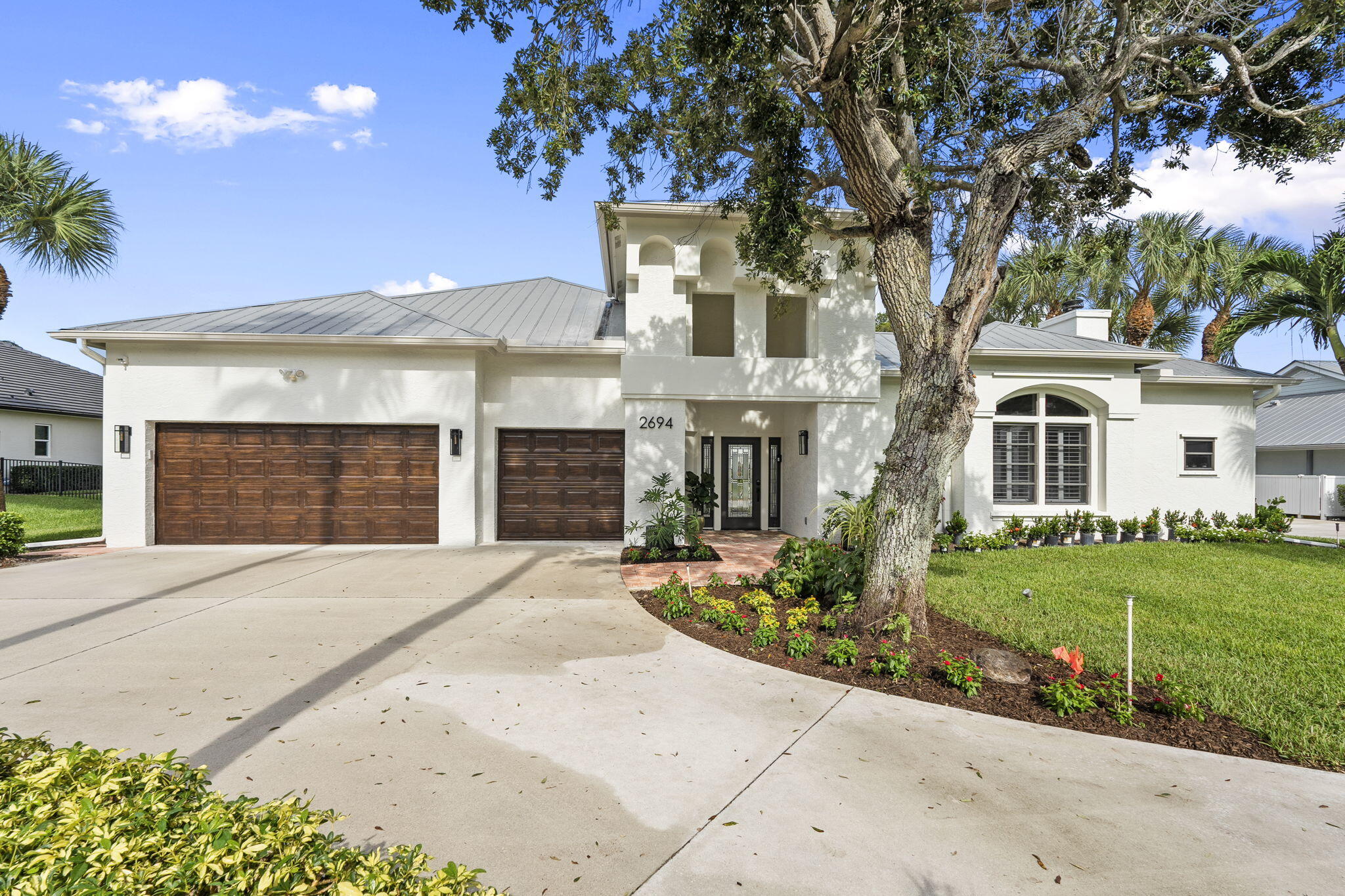 White modern home with two wood garage doors, a mature oak tree, and landscaped front yard.
