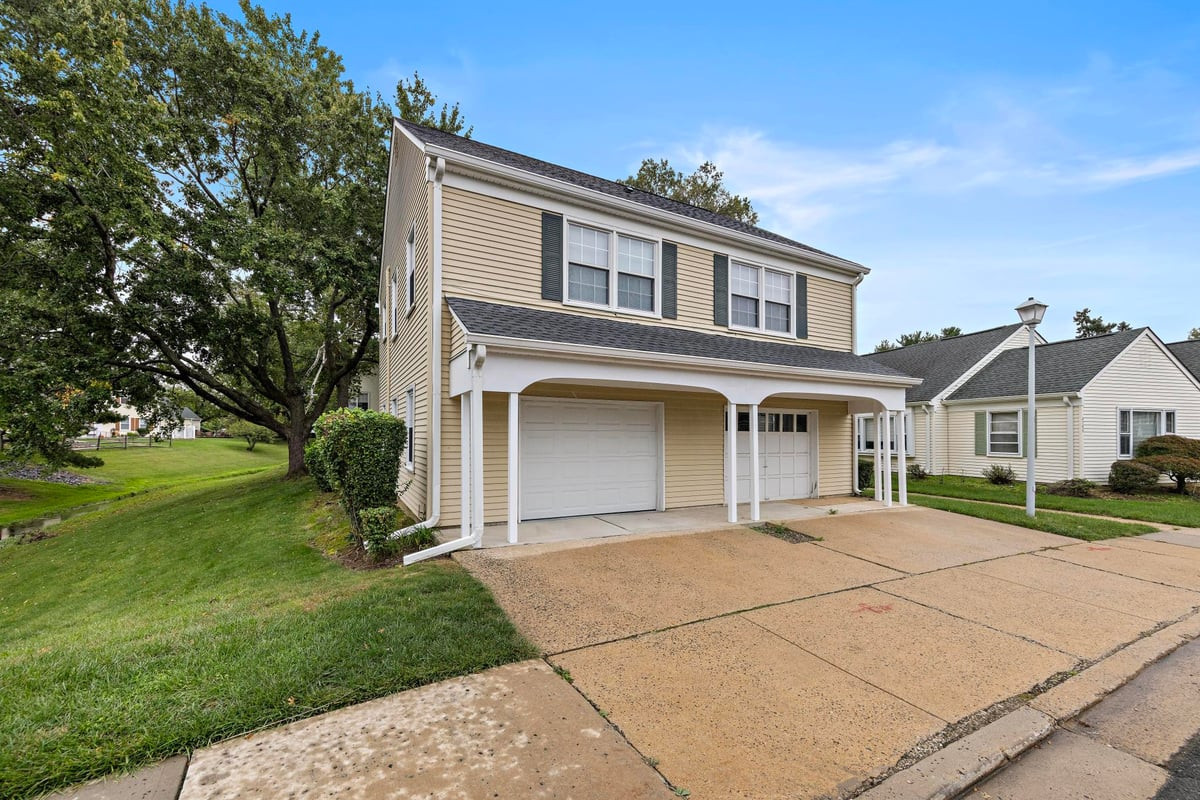 Two-story beige house with a covered garage entry and broad concrete driveway.