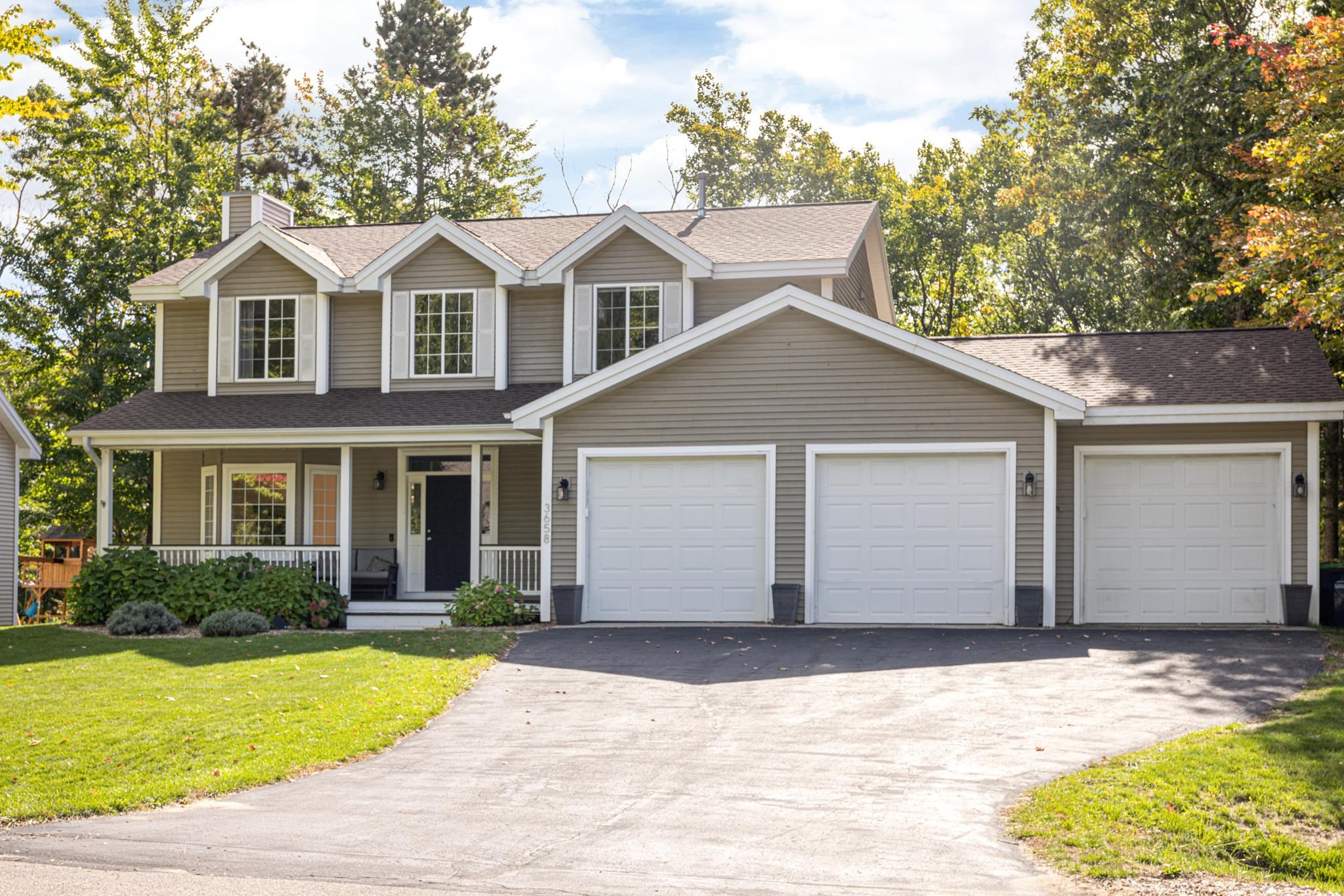 Two-story taupe house with a covered porch, three-car garage, and autumn trees.