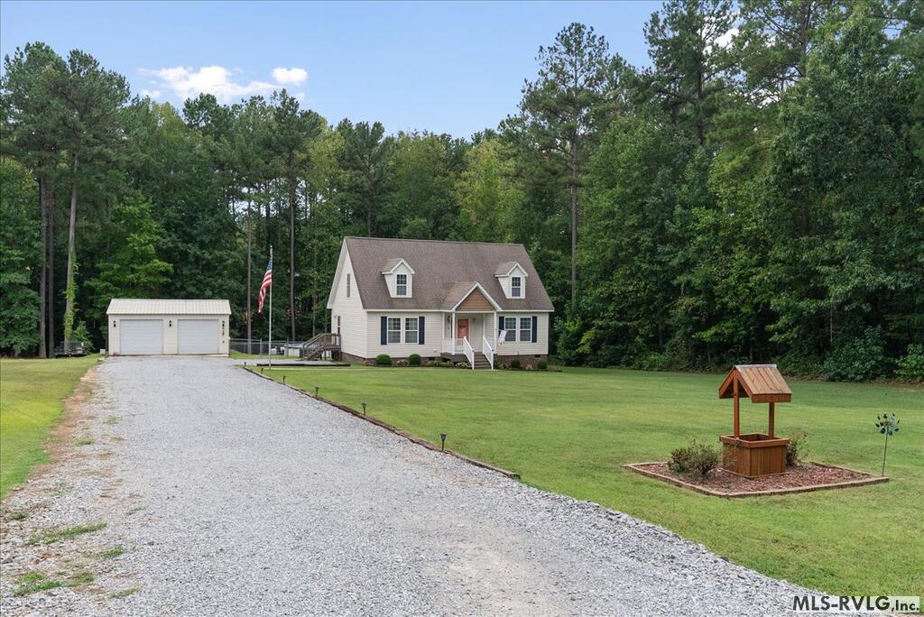 House with dormer windows, detached two-car garage, gravel driveway, broad lawn, and wooded surroundings.