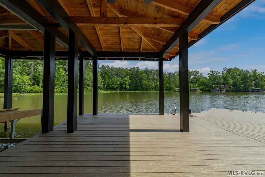 Covered lakeside dock with exposed wooden beams, a wide deck, and a tree-lined view across the water.