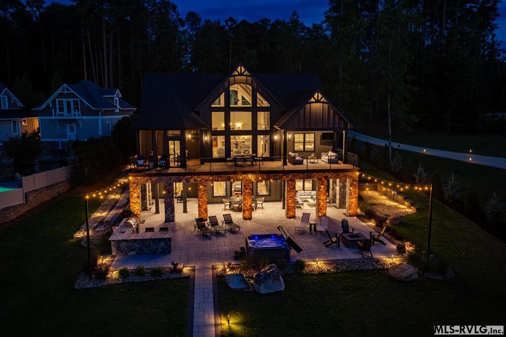Illuminated multi-level home with a stone patio, outdoor seating, and a hot tub at night.