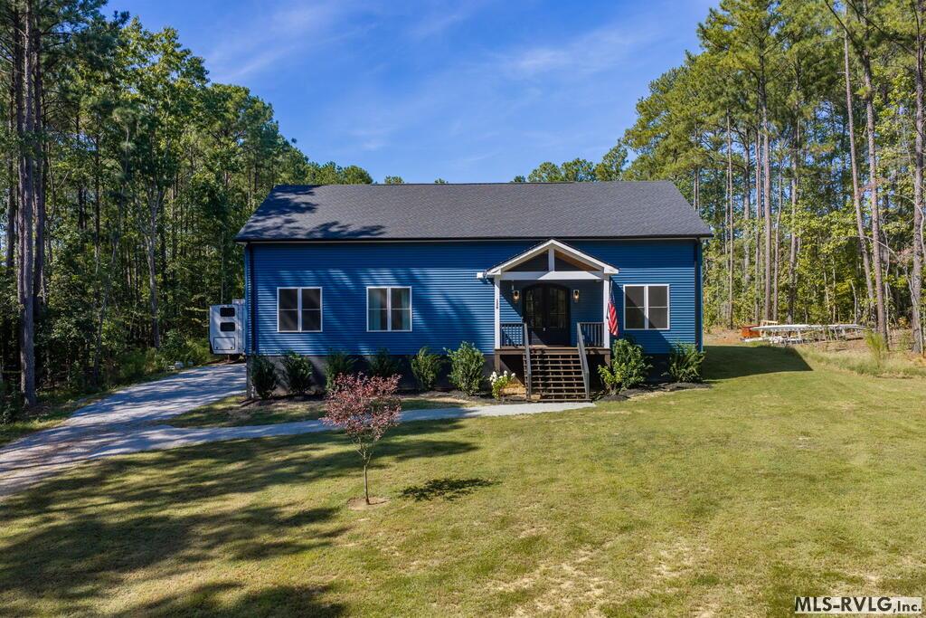 Blue single-story house with a covered front porch, driveway, and wooded surroundings.