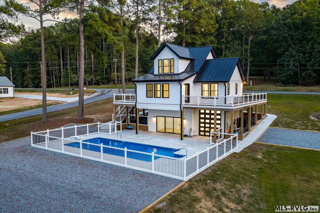 Modern white house with dark metal roofs, wraparound decks, and a fenced swimming pool.