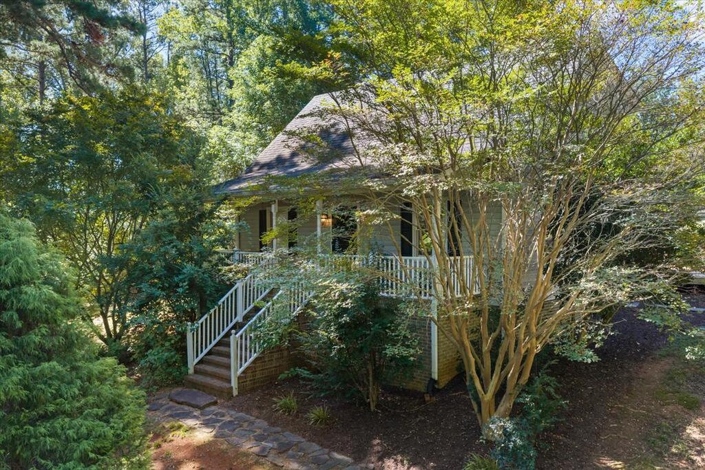 Brick-sided house with a white-railed porch, partly screened by mature trees and greenery.