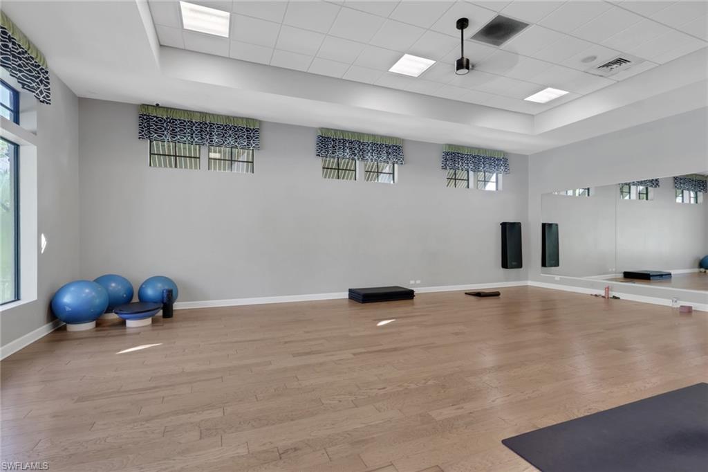 Exercise room with mirrored wall, light wood floors, exercise balls, and a yoga mat.