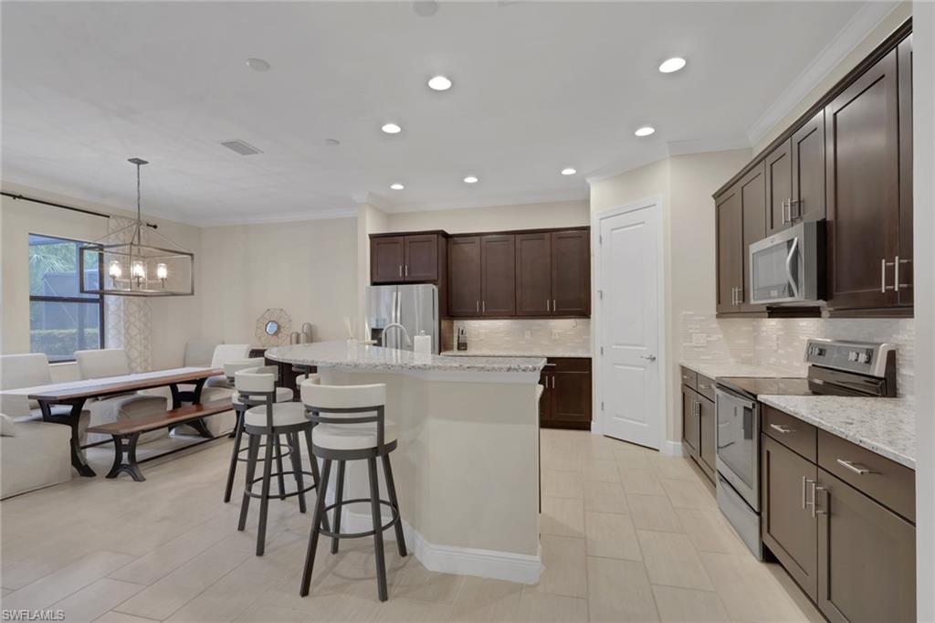 Kitchen with a large white island, dark wood cabinets, stainless steel appliances, and an adjoining dining area.