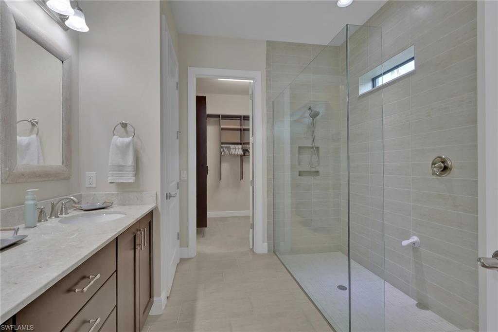 Primary bathroom with double vanity and glass walk-in shower beside an open closet doorway.