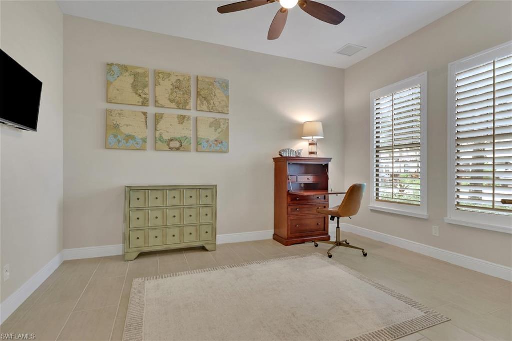 Furnished home office with a wooden writing desk, map prints, and two shuttered windows.