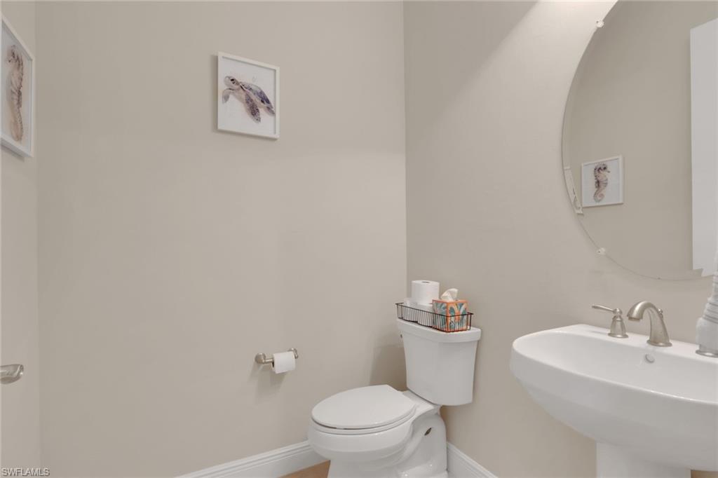 Bathroom with a white toilet, pedestal sink, round mirror, and framed sea-life artwork.