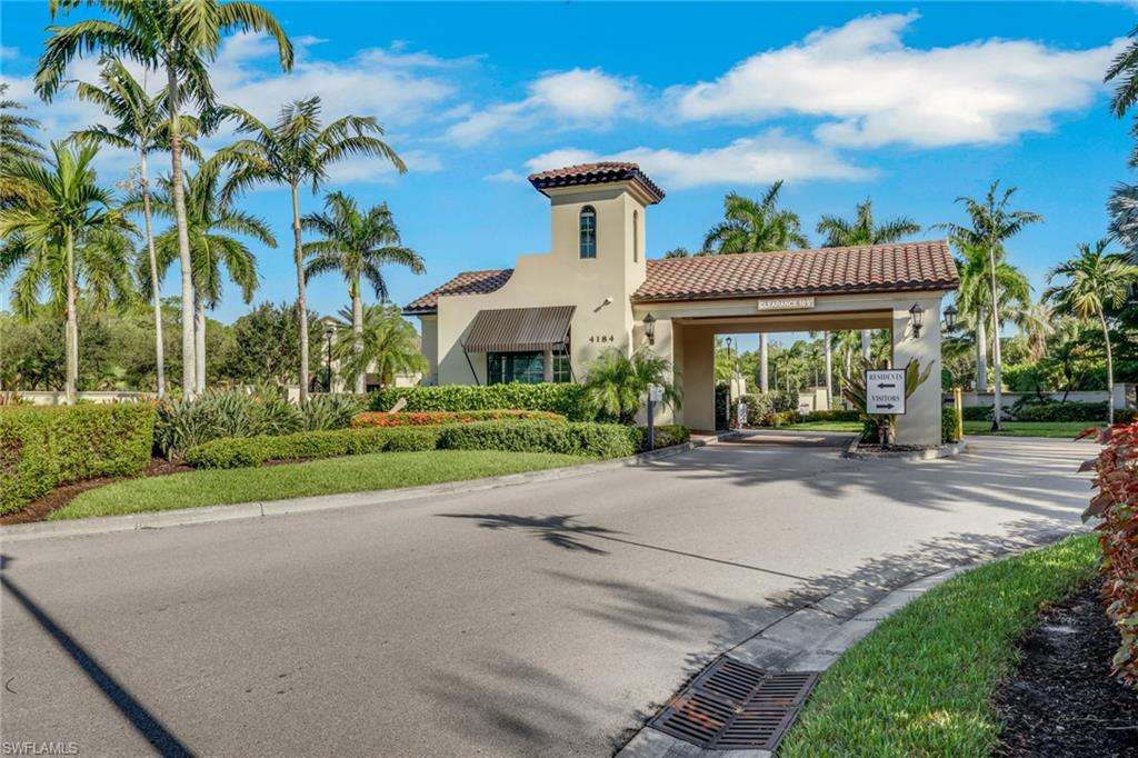 Gated community entrance with a cream guardhouse, terracotta tile roof, and palm trees.