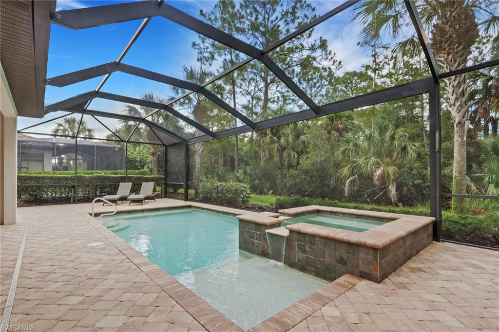 Screened pool and raised spa with paver deck, lounge chairs, and tropical landscaping.
