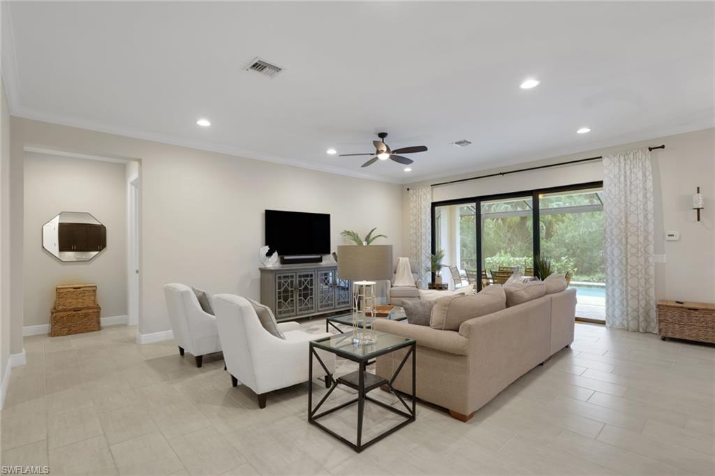 Furnished living room with a beige sectional, white armchairs, and sliding doors overlooking greenery.