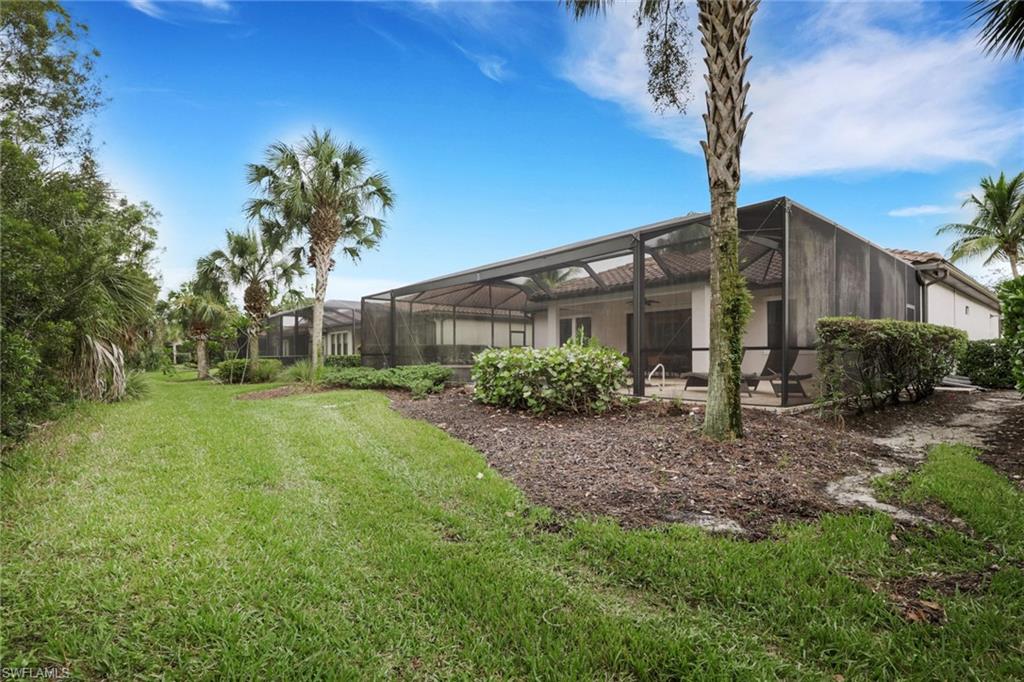 Rear of a home with a screened lanai, patio chairs, lawn, and palm trees.