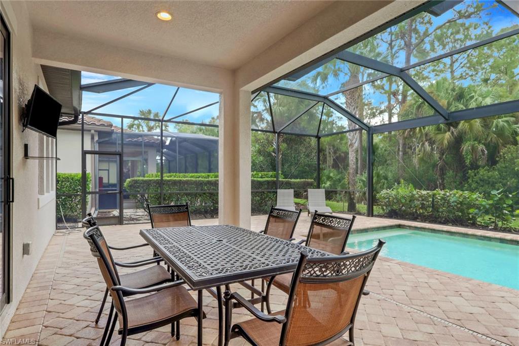 Screened lanai with patio dining set beside a swimming pool and tropical landscaping.