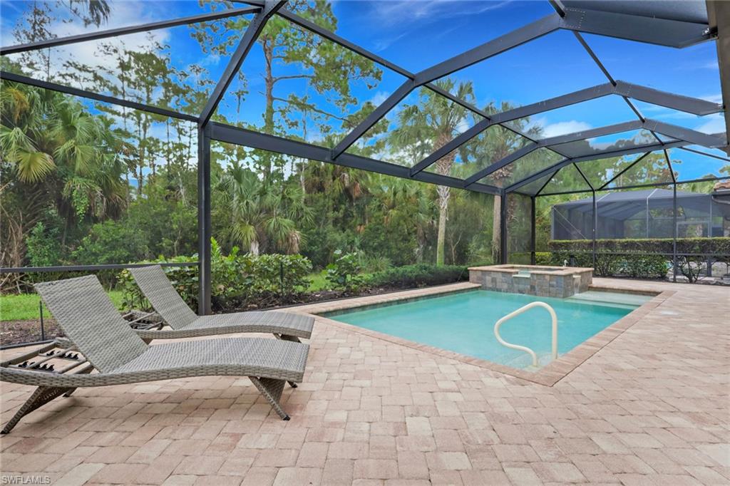 Screened backyard pool with a paver deck, woven lounge chairs, and tropical greenery.