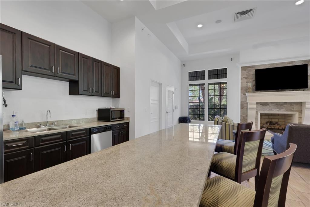 Kitchen and living area with a long granite island, dark cabinets, tall windows, and a stone fireplace.