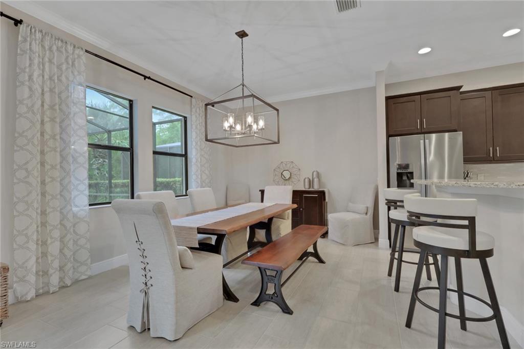 Dining area with a long wood table, geometric chandelier, and adjoining kitchen with dark cabinetry.
