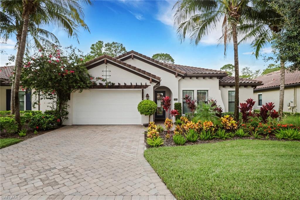 Single-story stucco home with a tiled roof, paver driveway, and lush tropical landscaping.
