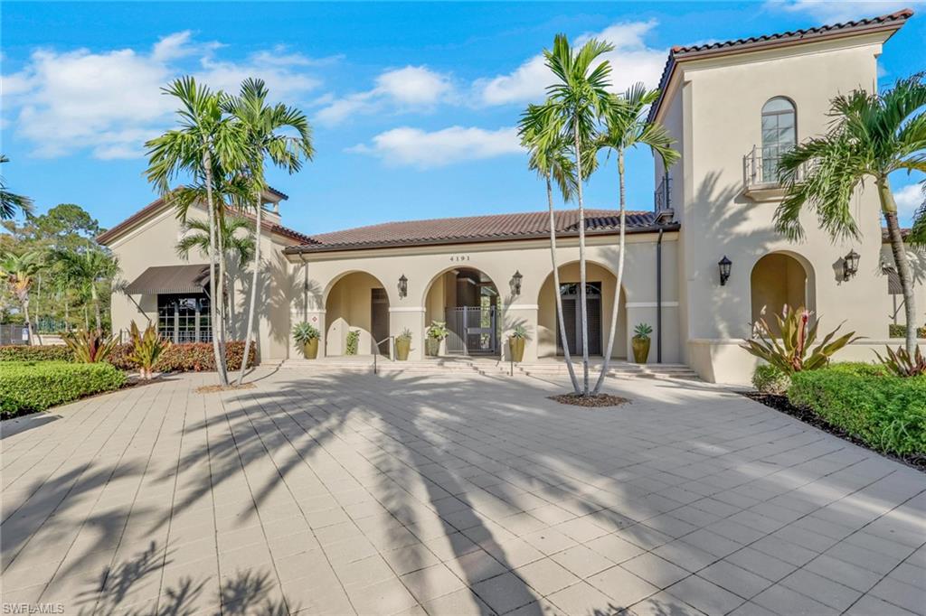 Cream stucco building with arched entrances, a tiled roof, and palm trees.
