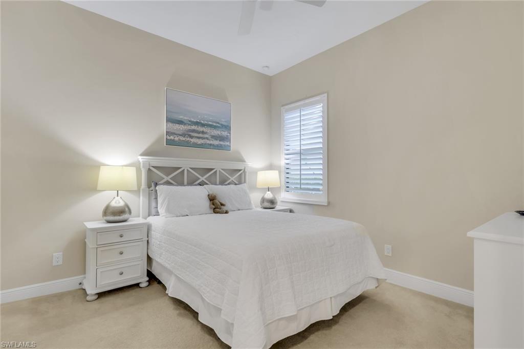 Staged bedroom with a white bed, matching nightstands, ocean artwork, and a shuttered window.