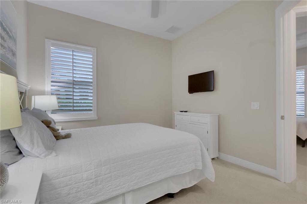 Bedroom with a white quilted bed, shuttered window, and wall-mounted television.