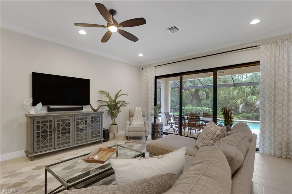 Living room with a large sectional and TV, opening to a screened lanai and pool.