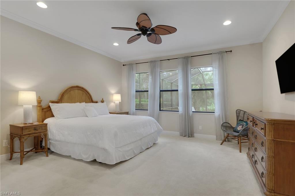 Bedroom with a white bed, wooden furniture, and three curtained windows overlooking greenery.