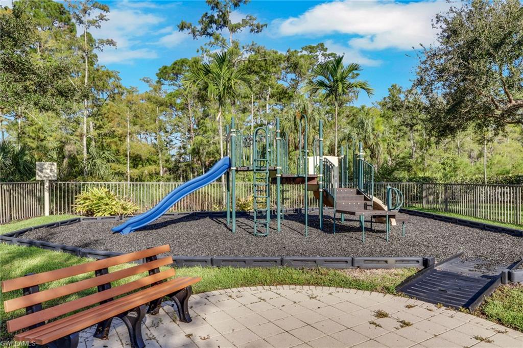Community playground with a blue slide, climbing equipment, and a wooden bench among trees.