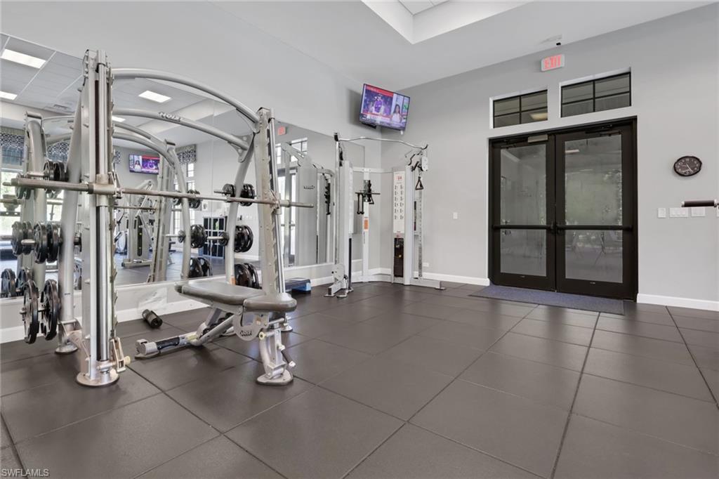 Fitness room with weight machines and mirrors beside black-framed glass doors.