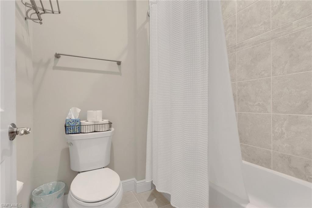 Bathroom with a white toilet beside a tiled bathtub and white shower curtain.