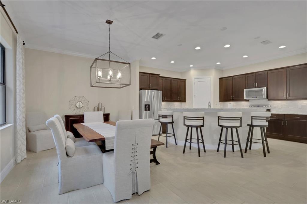 Open kitchen and dining area with dark wood cabinets, a white island, and a furnished dining table.