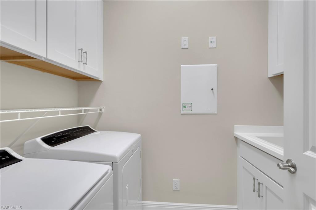 Laundry room with white washer and dryer, overhead cabinets, drying rack, and folding counter.