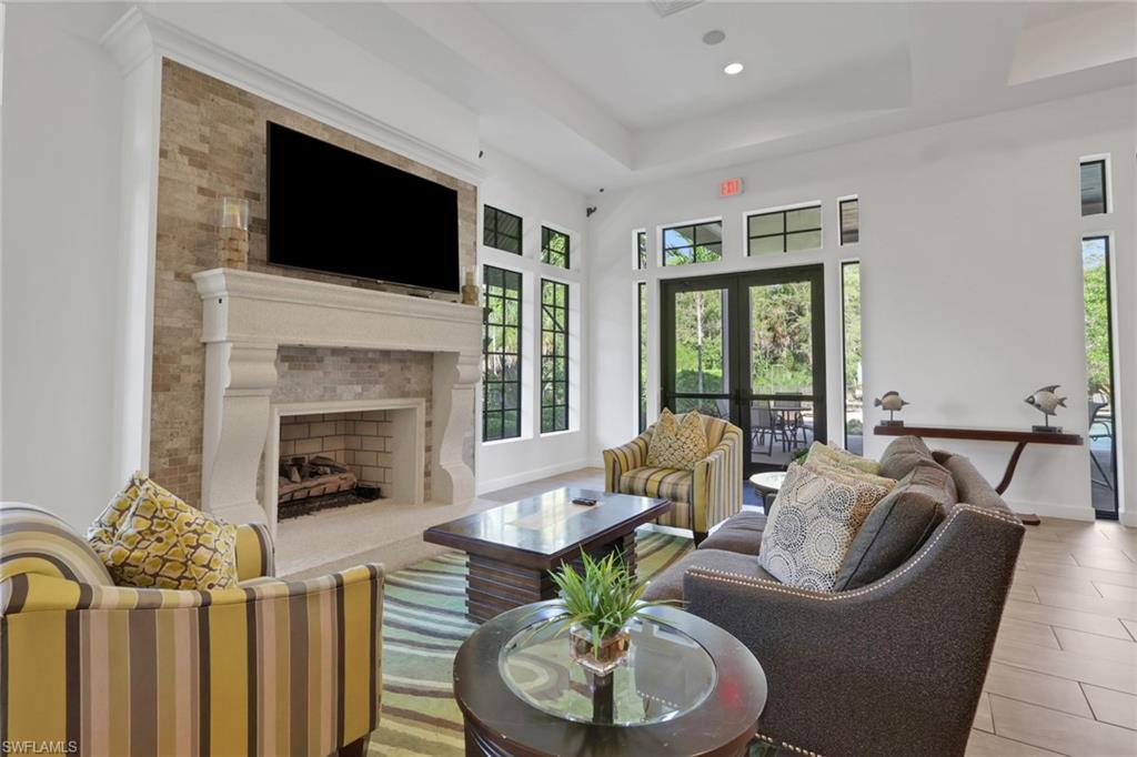 Furnished living room with a stone fireplace, mounted television, and tall windows beside patio doors.