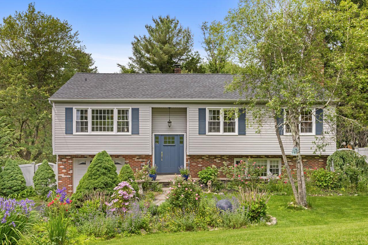 Split-level house with a blue front door, brick lower level, and colorful landscaped garden.