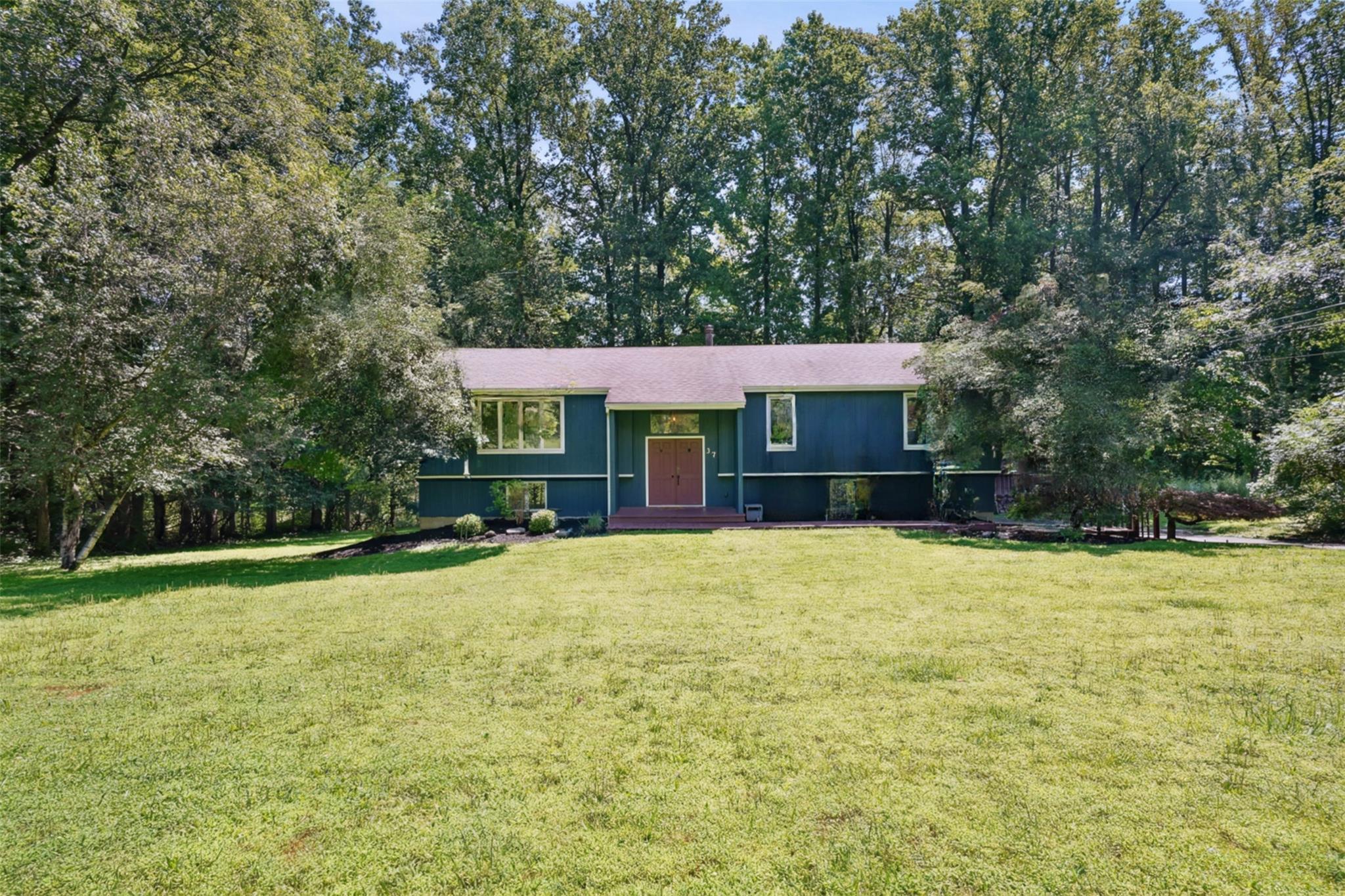 Blue house with a covered front entry, broad lawn, and mature trees.