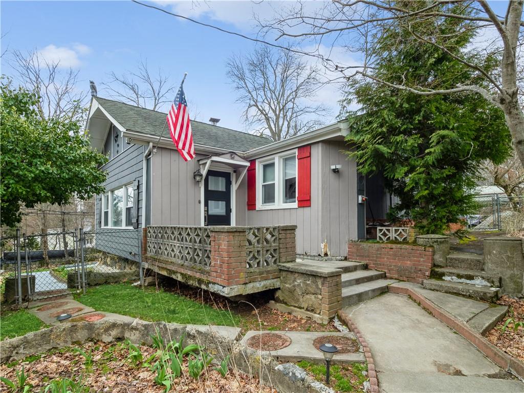 Gray single-story house with red shutters, an American flag, and stone front steps.
