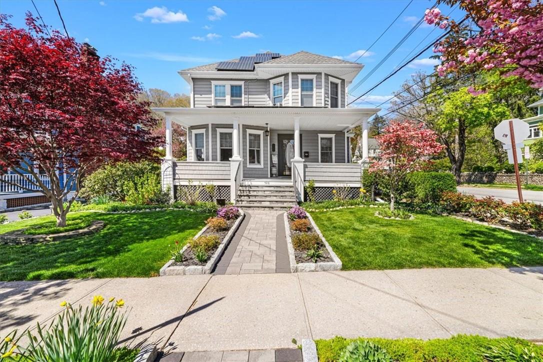 Gray two-story house with a wide porch, rooftop solar panels, and a landscaped front walkway.