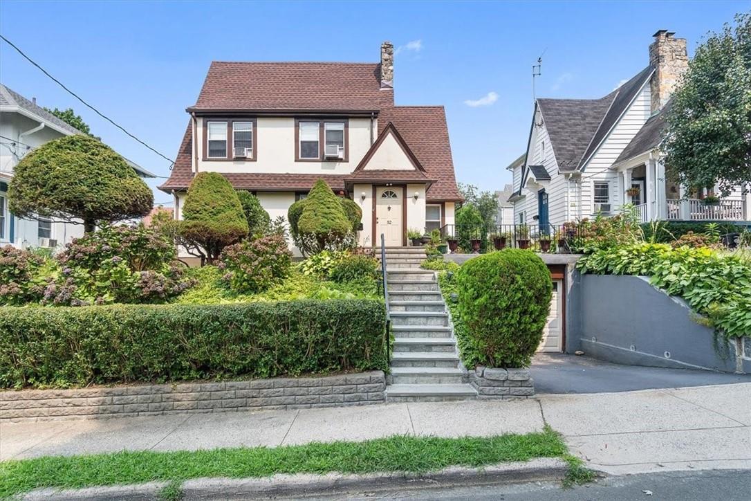 Two-story house with a steep brown roof, landscaped yard, stone steps, and driveway garage.