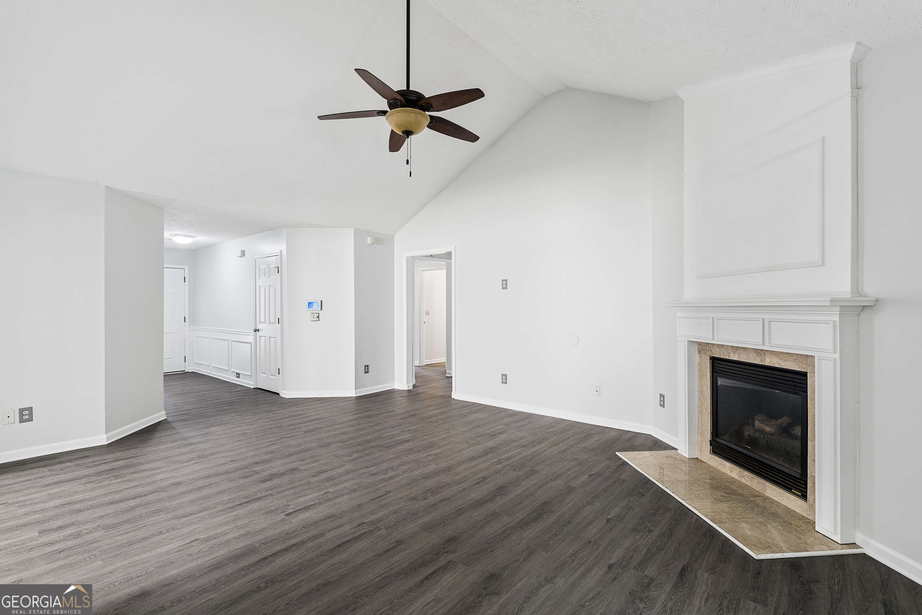 Vacant living room with vaulted ceiling, gray plank flooring, and a fireplace with a white mantel.
